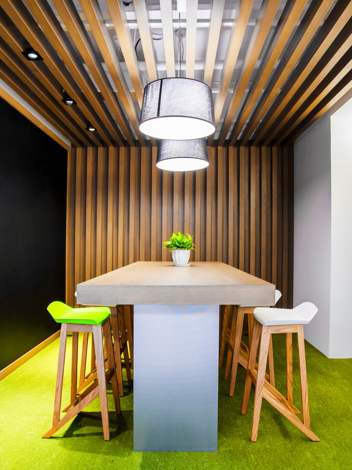 Image of table with a plant and 4 chairs. On a light green floor with wood bars to cover the wall