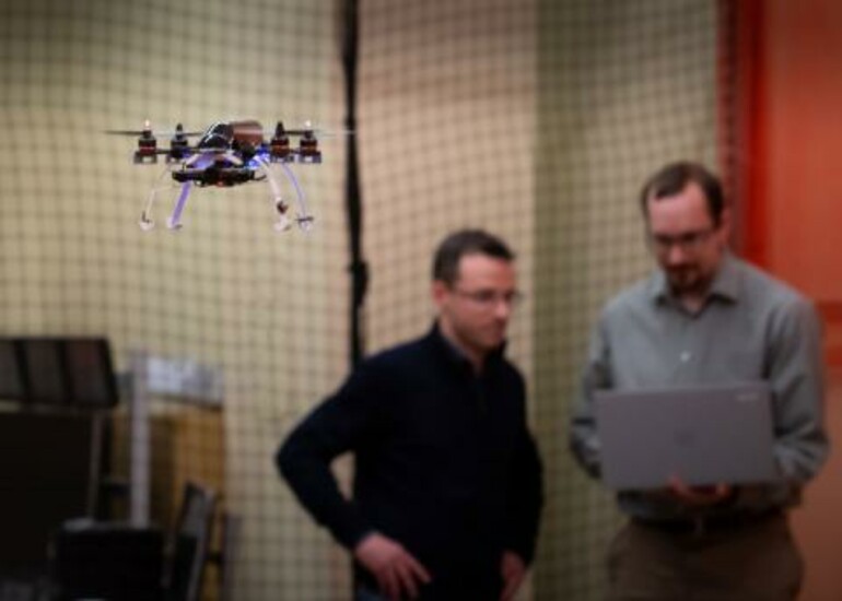 Autonomous drone in flight with two engineers monitoring its performance in the background.