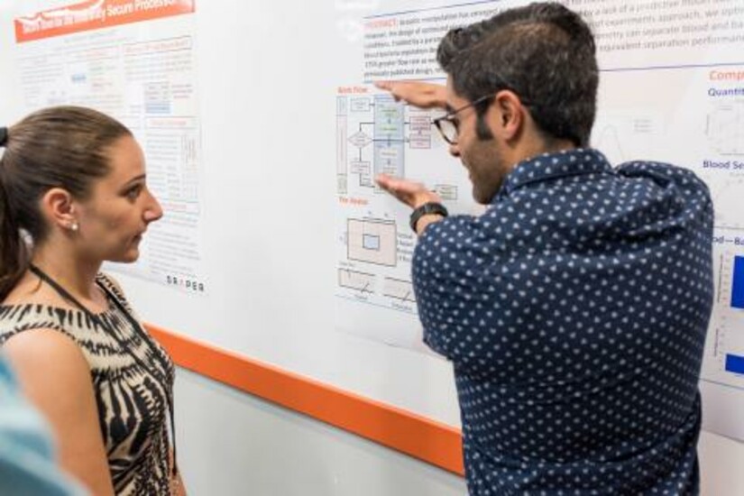Two Draper Fellow alumni discussing a technical poster at a conference.