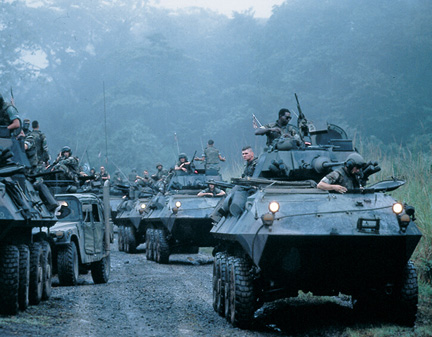 Military vehicles and soldiers navigate a muddy forest path, ready for action in a dense jungle setting.
