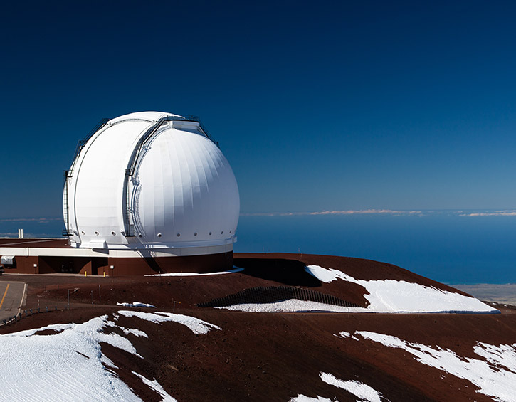 Large white observatory dome on a snowy mountain under a clear blue sky.
