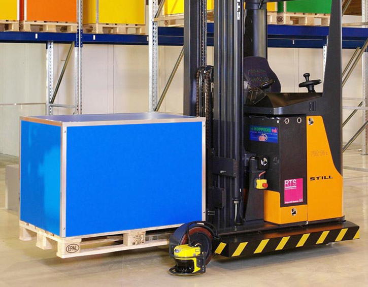 Forklift in a warehouse lifting a blue pallet box with colorful shelves in the background.