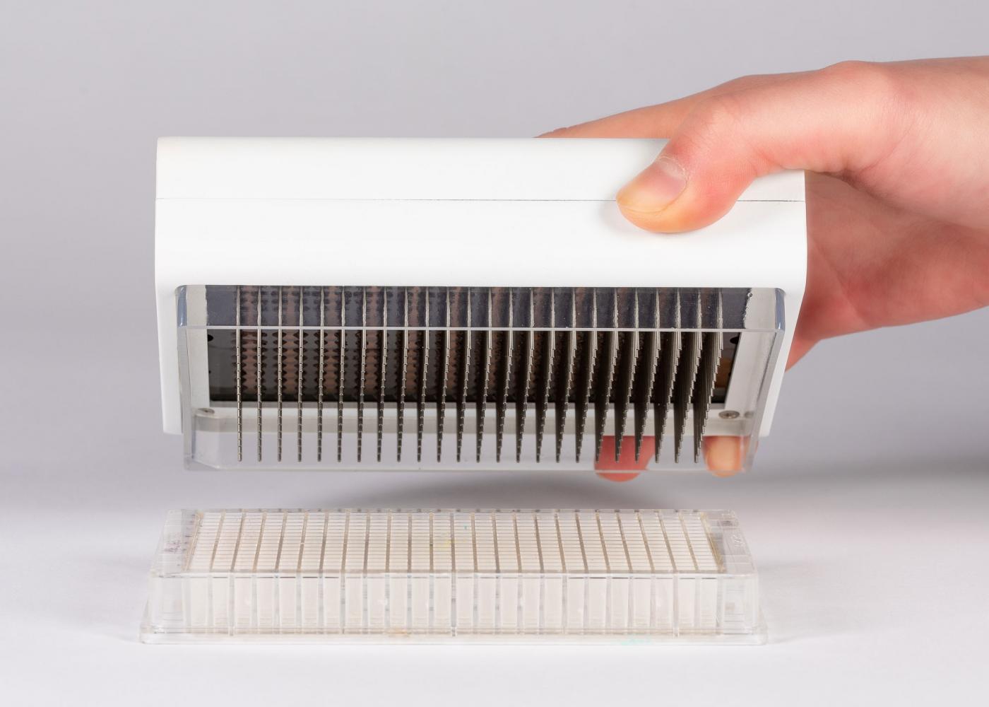 A hand holding PREDICT96, a white box with rows of metal rods, that is being held above a receptacle