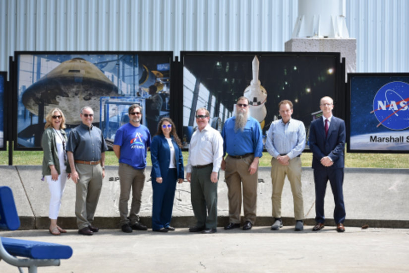Draper's Huntsville Team standing in front of NASA displays at Marshall Space Flight Center.