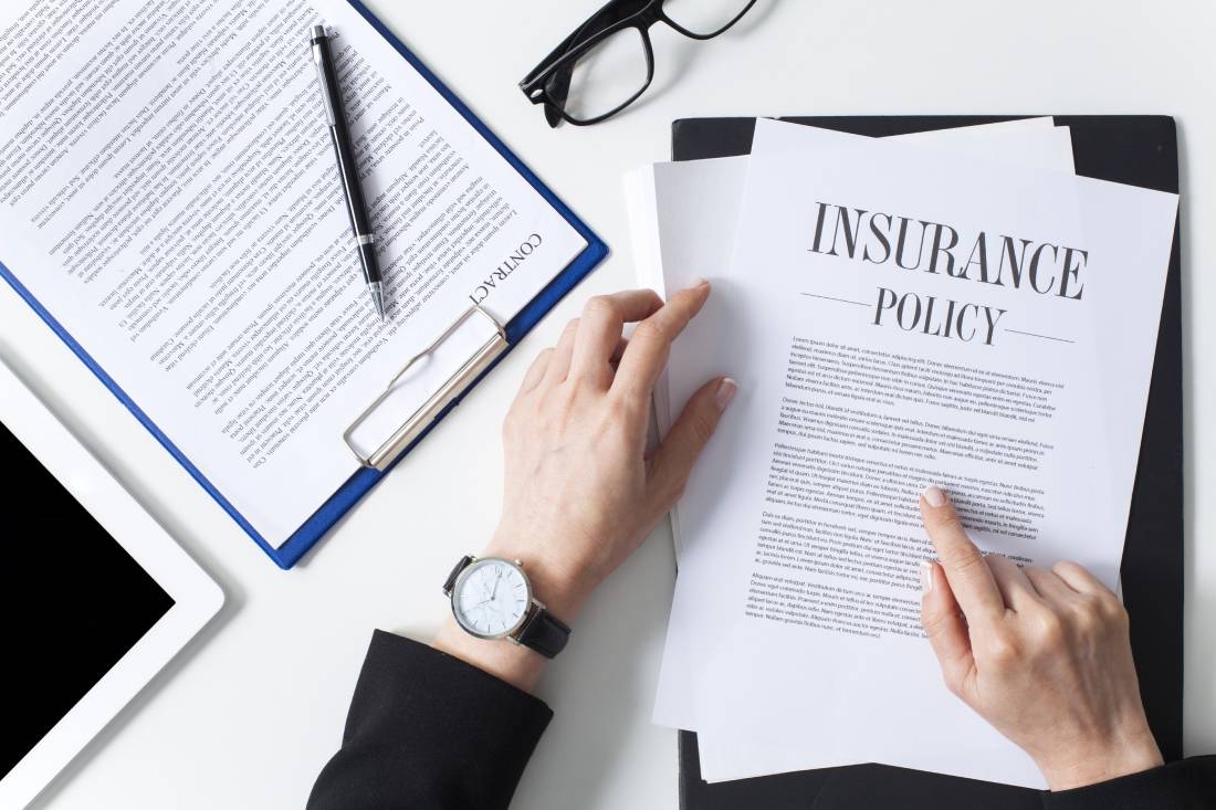 Clipboard with contract and a person holding a paper with "Insurance Policy" in the title