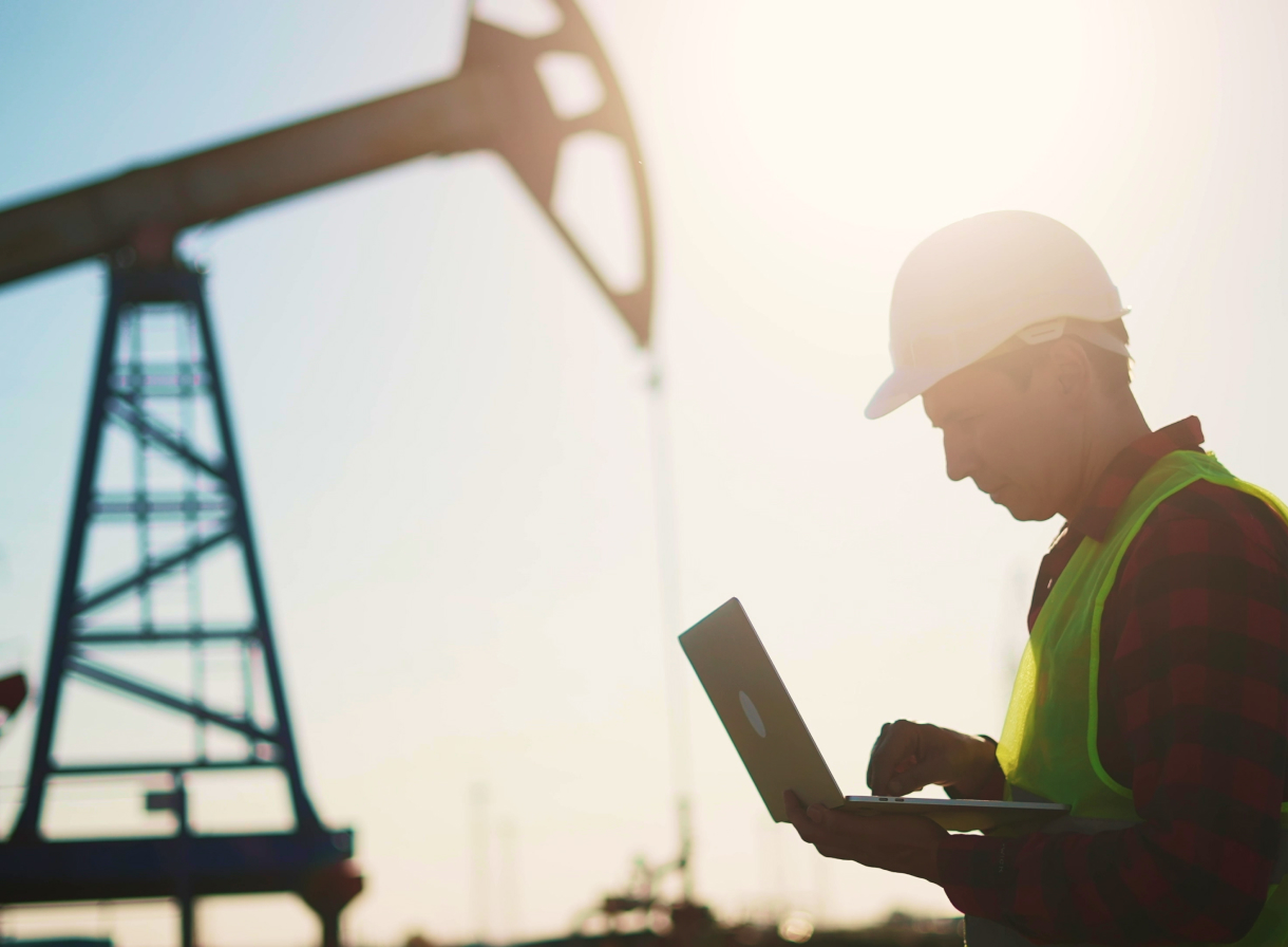 Construction worker looking at laptop, with a construction structure and the sun shown in the background