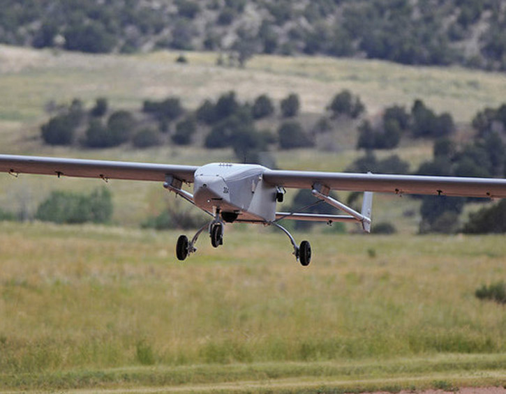 A drone flying low over a grassy field with trees in the background.