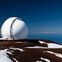 Large white observatory dome on a snowy mountain under a clear blue sky.