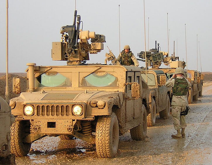 Military convoy of armored vehicles with soldiers on a muddy road.