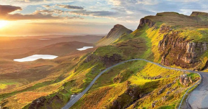 A road winding through a lush green landscape of mountains and cliffs.