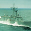 A naval warship cruising through the ocean with waves splashing against its hull.