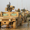 Military convoy of armored vehicles with soldiers on a muddy road.