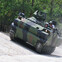 Military tank navigating a steep incline in a forested area.