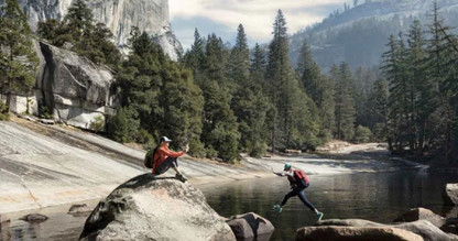 Two people among the wilderness taking photos and jumping over a river.