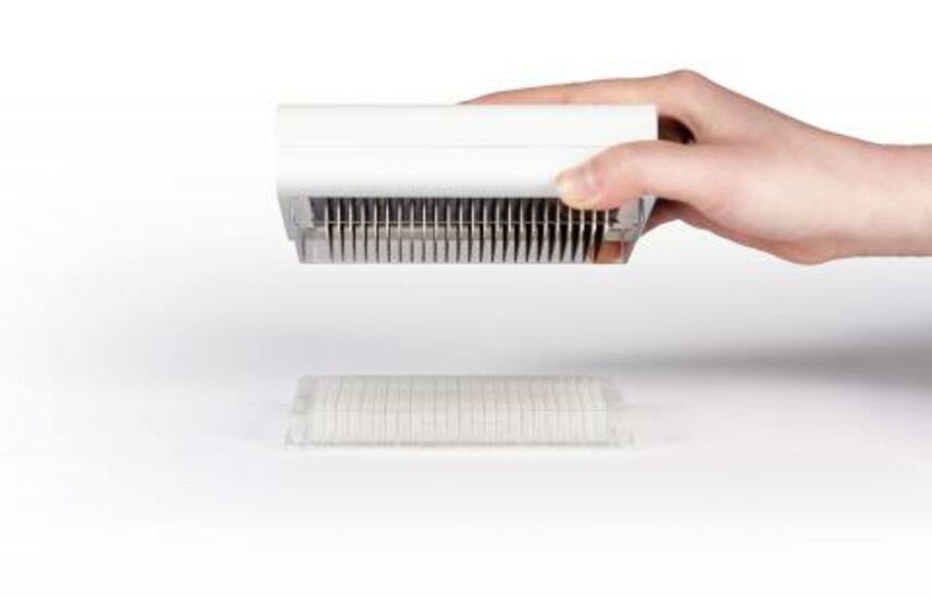 A hand holding a white device above a transparent object on a white surface.