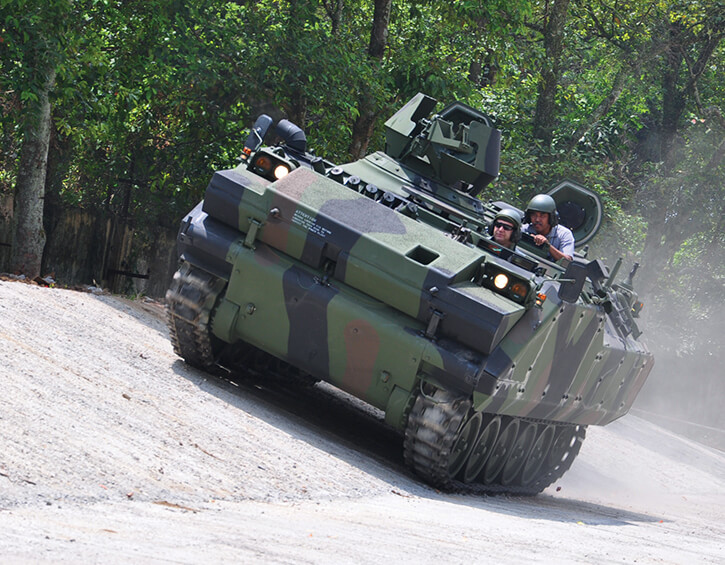 Military tank navigating a steep incline in a forested area.