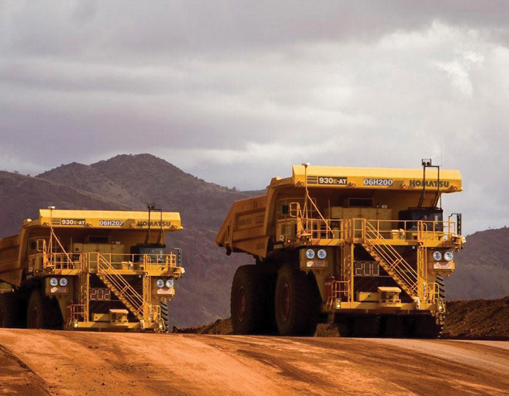 Two large yellow mining trucks on a dirt road with mountains in the background.