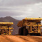 Two large yellow mining trucks on a dirt road with mountains in the background.