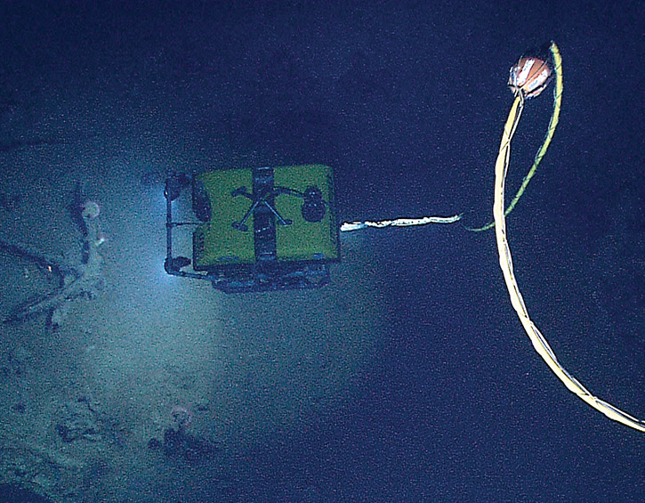 Underwater ROV exploring the ocean floor with a tether cable and light illuminating the surroundings.
