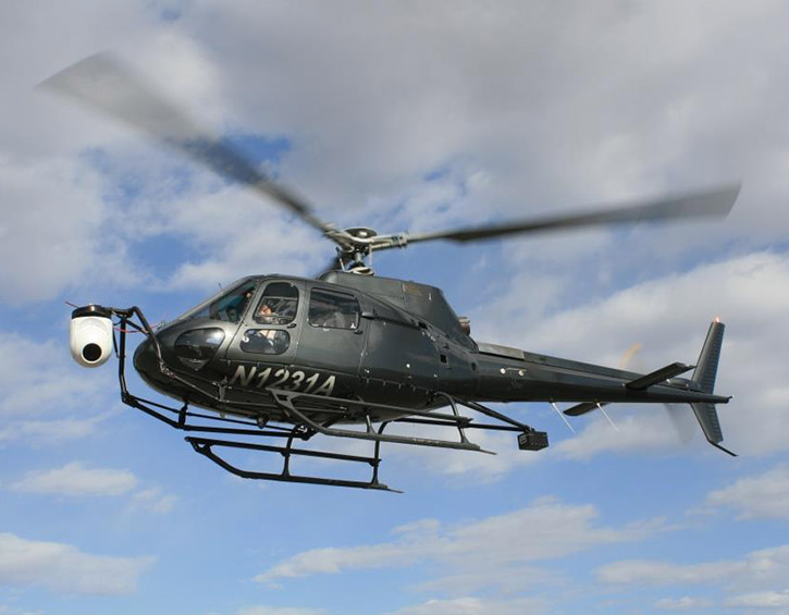 A black helicopter with registration N1231A flying against a cloudy sky.