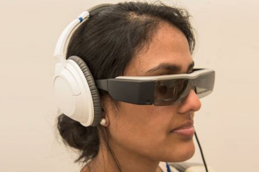 Person wearing augmented reality glasses with heads-up display and 3D audio headphones.