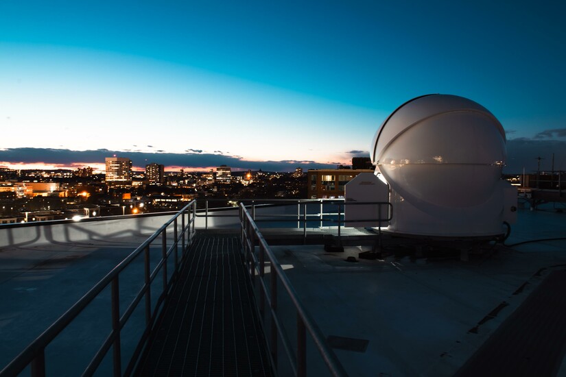 Observatory dome at dusk with city skyline, supporting celestial navigation programs.