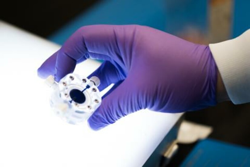 A gloved hand holds Draper's Microfluidic Transduction Module