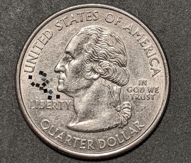 Close-up of a U.S. quarter dollar with tiny black squares near the word "LIBERTY" on the coin.