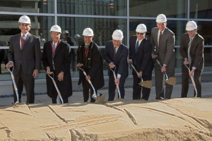 Officials participate in a groundbreaking ceremony, each holding a shovel and wearing hard hats.