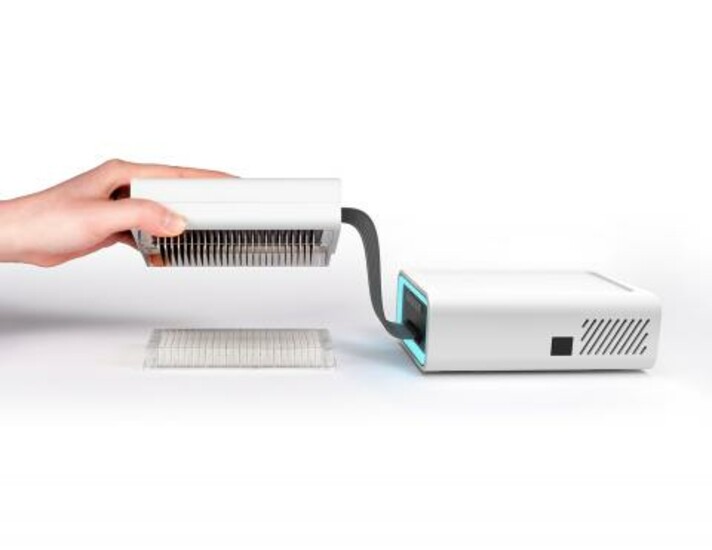 PREDICT96 device, two white boxes connected with a cable while one person holds one of the boxes above a transperent object