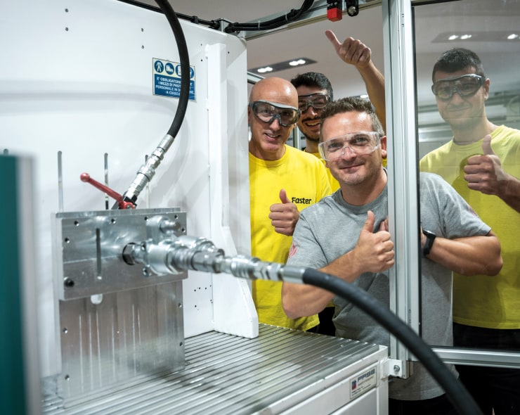 Four employees giving a thumbs up wearing protective glasses around equipment
