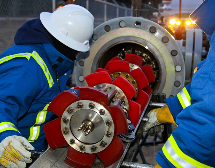 Workers in safety gear inspect a pipeline pigging tool at an industrial site.