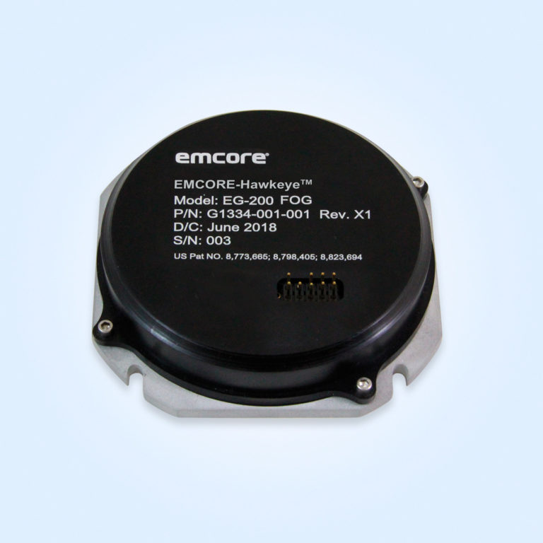 A circular device with a black top and silver bottom. The label reads: EMCORE-Hawkeye EG-200 FOG, model G1334-001-001, manufactured in June 2018.