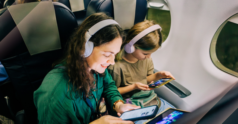 Woman and girl wearing headphones and looking at phones on an airplane