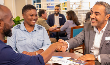 Two men of color shaking hands while a woman of color smiles beside them.