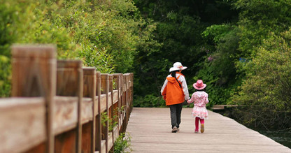 An adult woman and little girl holding hands as they walk along a boardwalk.