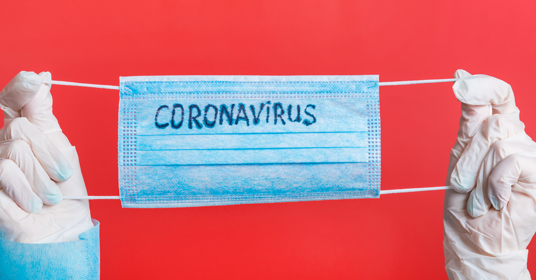 Person wearing protective gear, holding mask with "coronavirus" printed on it