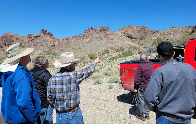 Man pointing at hill with other men and pickup truck
