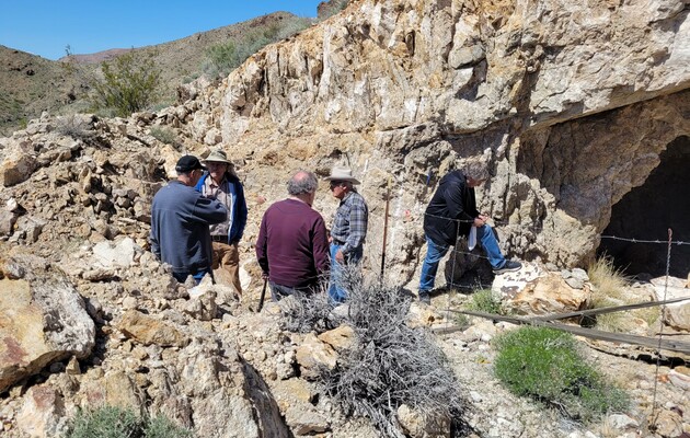 Men standing by rocky cave protected by barbed wire fence