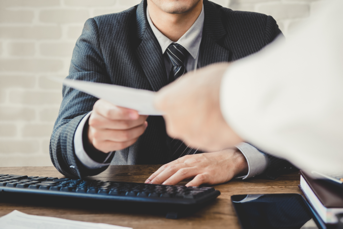 Man sitting at a desk while another person hands them a document
