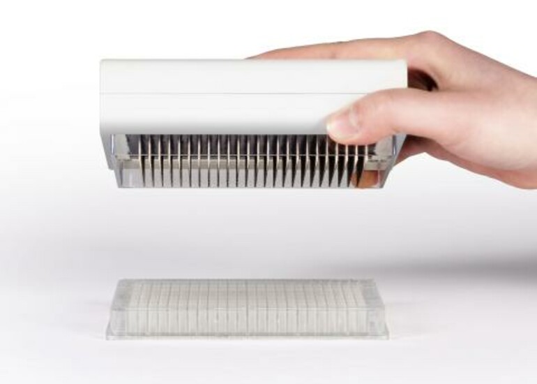 A hand holds Draper’s PREDICT-96 device above a sample tray 
