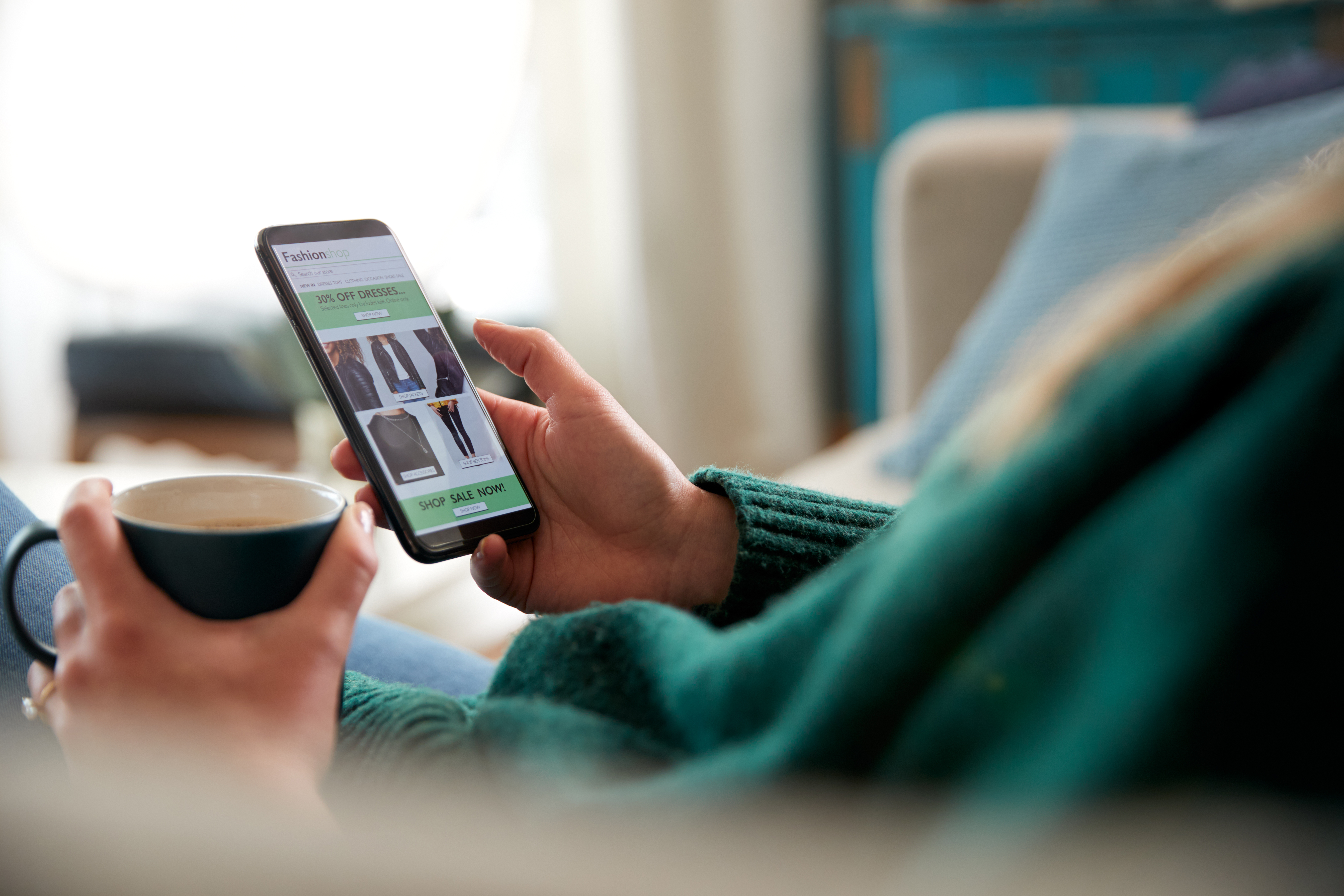An over the shoulder image of a person browsing their phone with a drink in hand.